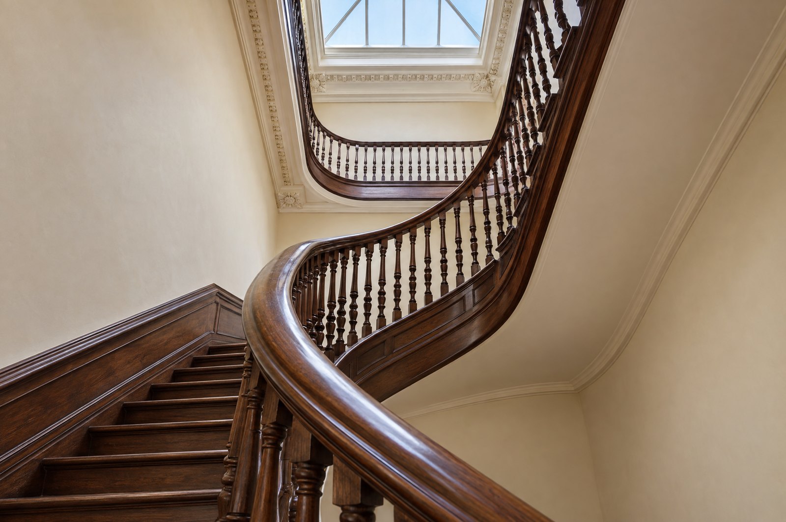 A restored walnut staircase with turned balusters rising toward a skylight